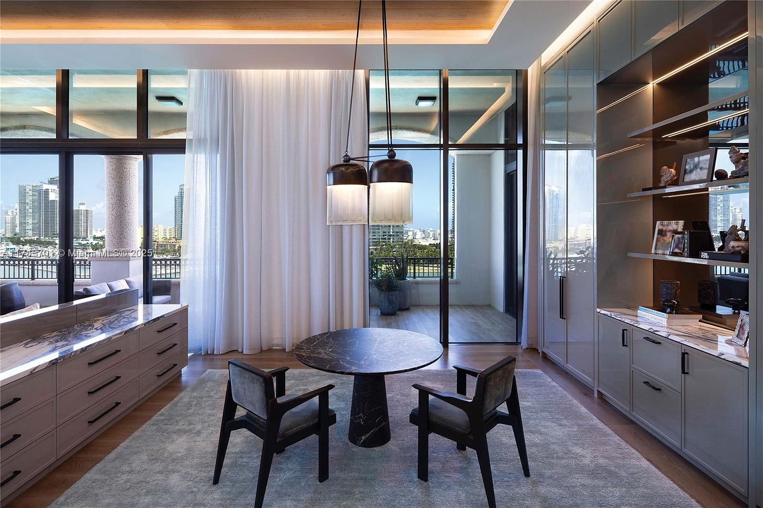 This interior shot showcases a modern dining area with a round marble table and two stylish chairs set on a gray rug. Natural light floods the room through large windows, offering a city view, while pendant lights hang above the table. Built-in cabinetry with display shelves adds a touch of elegance and functionality to the space.