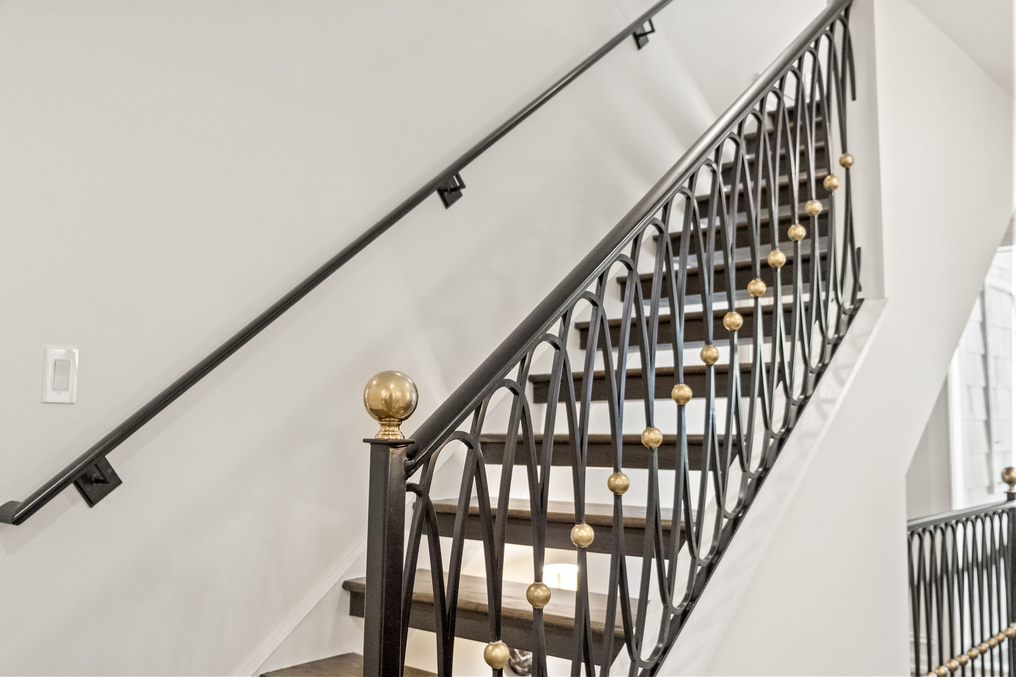 This image showcases a staircase with dark wood steps and an ornate black iron railing accented with gold spheres. The railing's design features curved vertical elements, adding a touch of elegance to the interior. The walls are painted in a neutral tone, and the overall impression is one of sophisticated design and quality craftsmanship.