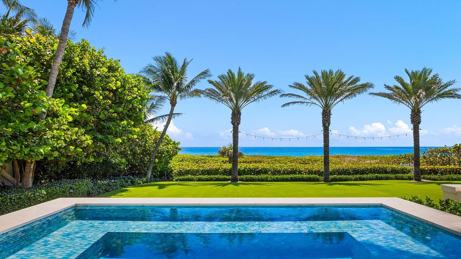 This image showcases a luxurious pool area with a stunning ocean view. The pool features a tiled interior and a clean, modern design. Palm trees line the horizon, creating a tropical and serene atmosphere, perfect for relaxation and entertainment.