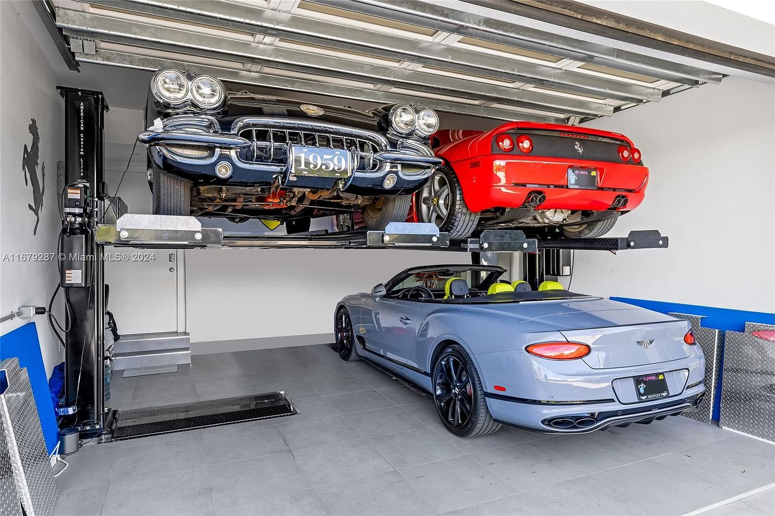 This image showcases a well-organized garage featuring a car lift system with a classic black 1959 car and a red Ferrari on the lift, and a light blue Bentley convertible parked below. The garage has a clean, modern aesthetic with light gray flooring and white walls, suggesting a high-end, luxury space for car enthusiasts.