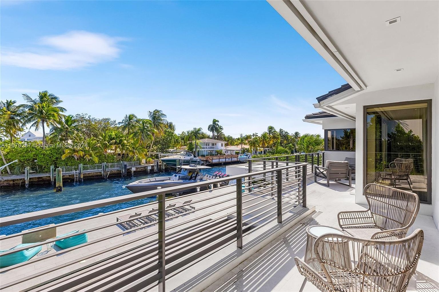 This image showcases a luxurious balcony overlooking a waterfront property. The balcony features modern railings, stylish outdoor seating, and a view of a boat docked along the canal. Lush greenery and clear blue skies enhance the appeal of this outdoor living space, perfect for relaxation and entertainment.