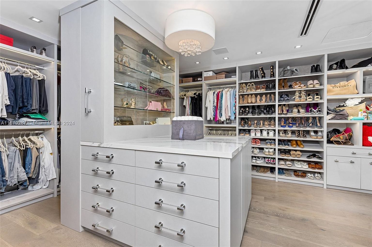 This is a well-organized walk-in closet featuring custom shelving and drawers. The closet includes sections for hanging clothes, shoes, and accessories, all illuminated by recessed lighting and a decorative chandelier. The overall impression is luxurious and efficient, maximizing storage space.