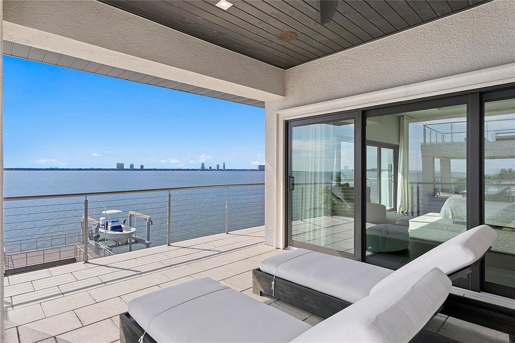 This image showcases a luxurious balcony with stunning waterfront views. The balcony features modern lounge chairs, a sleek railing system, and seamless access to the interior through large sliding glass doors. The overall impression is one of sophisticated relaxation and seamless indoor-outdoor living.