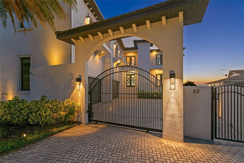 This image showcases the grand entryway of a luxurious property, featuring an arched gate and a meticulously paved driveway. The architectural design includes elegant lighting fixtures and a well-maintained garden, creating a welcoming and sophisticated first impression. The perspective is from a low angle, emphasizing the height and grandeur of the entrance.