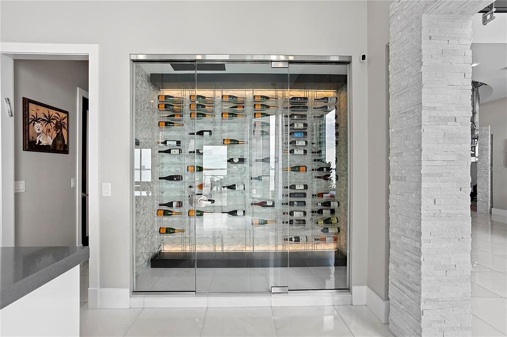 This interior shot showcases a modern wine cellar with a glass-enclosed display. The cellar features a sleek, minimalist design with rows of wine bottles displayed on clear shelves against a textured wall. The space is well-lit, highlighting the collection and creating an elegant ambiance.