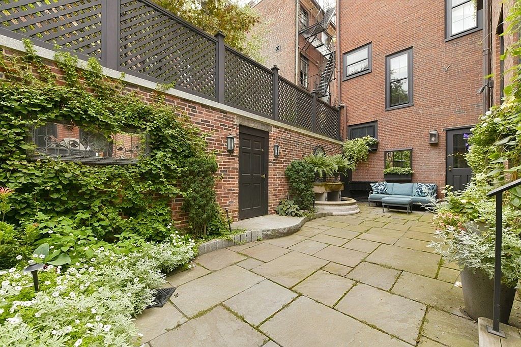 This image showcases a charming courtyard garden, featuring a stone-paved patio, lush greenery, and a brick wall adorned with climbing vines. A small fountain adds a touch of elegance, while a cozy outdoor seating area invites relaxation. The overall impression is one of a private and serene outdoor space.