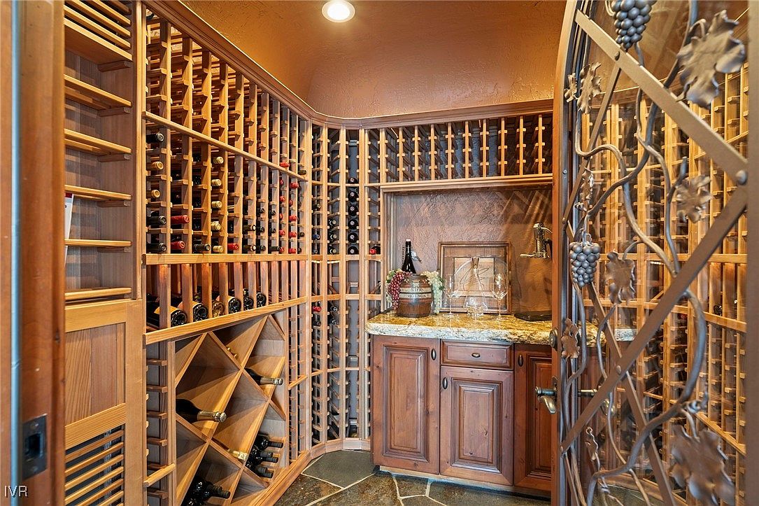 This is a well-appointed wine cellar featuring extensive wooden racking for numerous bottles. A countertop area with cabinetry provides space for serving and display, complemented by decorative elements. The wrought iron gate adds a touch of elegance and security to the space.