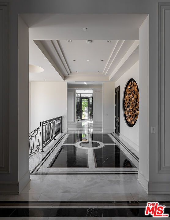 This interior shot showcases a luxurious hallway with a striking black and white marble floor design. The hallway features elegant architectural details, including paneled walls and a decorative oval wall art piece. The perspective emphasizes the depth and grandeur of the space, leading the eye towards a doorway at the end of the hall.