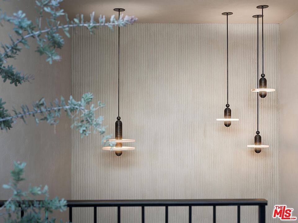 This interior shot showcases a modern hallway or stairwell area featuring three pendant lights with a unique, minimalist design. The walls have a textured, vertical pattern, and a black railing is visible in the foreground. The overall aesthetic is clean, contemporary, and well-lit, creating a sophisticated and inviting atmosphere.
