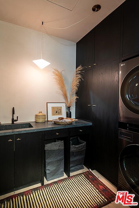 This is a modern laundry room featuring dark cabinetry and countertops, complemented by a light-colored wall. The room includes a sink, a washer and dryer set, and decorative elements such as pampas grass and a framed picture. A striped rug adds a touch of warmth to the space.