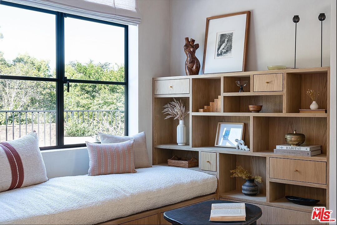 This interior shot showcases a cozy living space with a built-in window seat and a custom wooden shelving unit. The window provides natural light and a view of the outdoors, while the shelving unit displays various decorative items. The overall aesthetic is warm, inviting, and stylish, perfect for a comfortable living area.