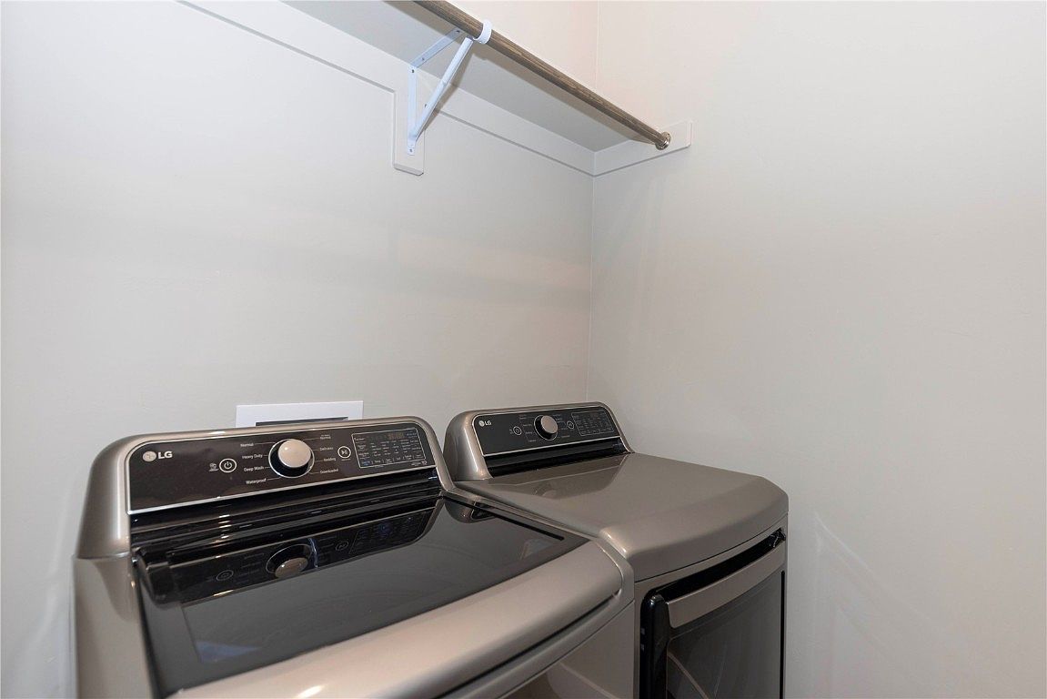 This interior shot showcases a laundry room featuring a modern LG washer and dryer set in a neutral gray tone. Above the appliances, a simple metal rod with white brackets provides hanging space. The walls are painted in a light, complementary color, creating a clean and functional space.