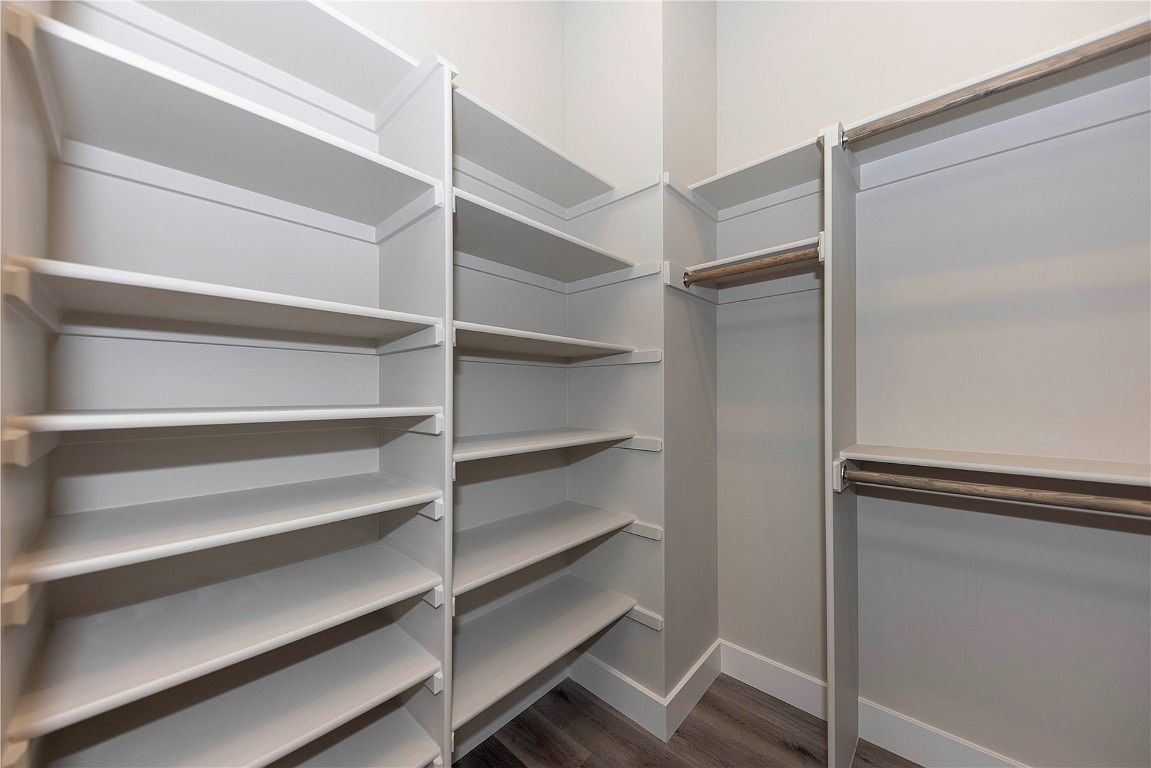 This is a well-organized walk-in closet featuring custom white shelving and hanging rods. The closet is spacious and offers ample storage for clothing and accessories. The flooring appears to be a modern wood-look laminate, and the overall impression is clean and functional.