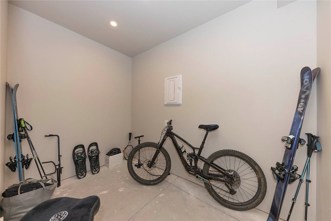 This is an interior shot of a garage or storage room, showcasing a practical space for outdoor equipment. The room features a mountain bike, skis, snowshoes, and other sporting gear neatly arranged against the walls. The neutral color palette and clean lines create a functional and organized area, perfect for active homeowners.
