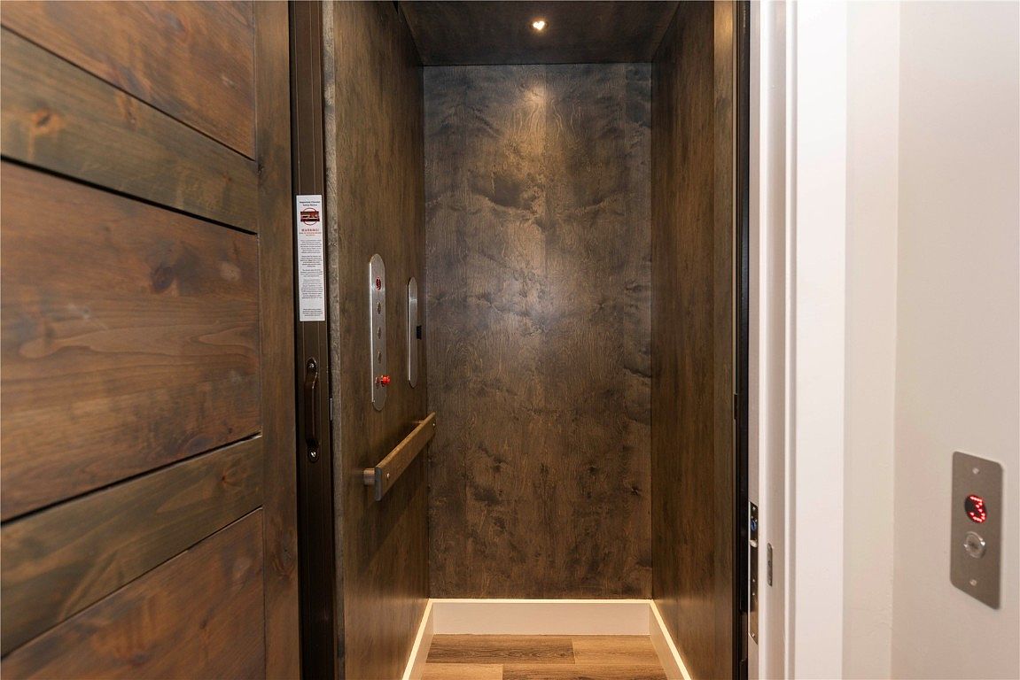 The image showcases the interior of a residential elevator. The elevator features wood-paneled walls, a control panel, and subtle lighting, creating a modern and functional design element within the home. The floor has a wood-like pattern, and the overall impression is one of convenience and luxury.