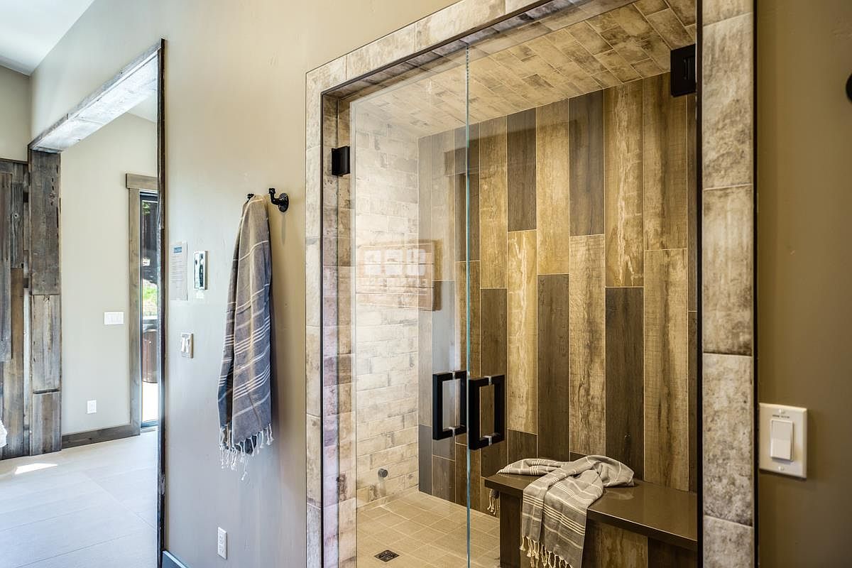 This is a primary bathroom featuring a glass-enclosed shower with a built-in bench. The shower walls are tiled with a mix of light and dark wood-look planks, creating a modern and spa-like atmosphere. A gray striped towel hangs on a hook outside the shower, adding a touch of comfort and style.