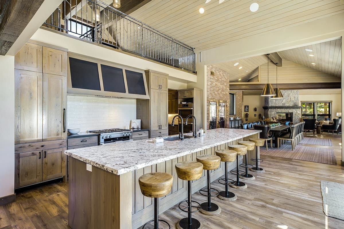 This is a spacious, open-concept kitchen featuring a large island with bar seating, light wood cabinetry, and granite countertops. The kitchen is well-lit and flows seamlessly into the dining and living areas, creating an inviting space for entertaining. A unique architectural feature is the upper-level balcony overlooking the kitchen.