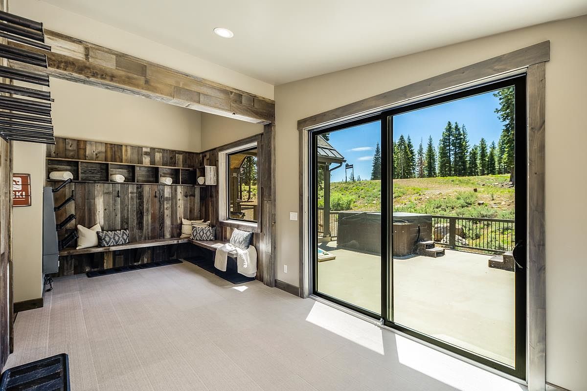 This interior shot showcases a home gym area with rustic wood paneling and built-in shelving. A large sliding glass door provides access to an outdoor patio with a hot tub, offering a seamless transition between indoor and outdoor spaces. The room features a neutral color palette and natural light, creating a serene workout environment.