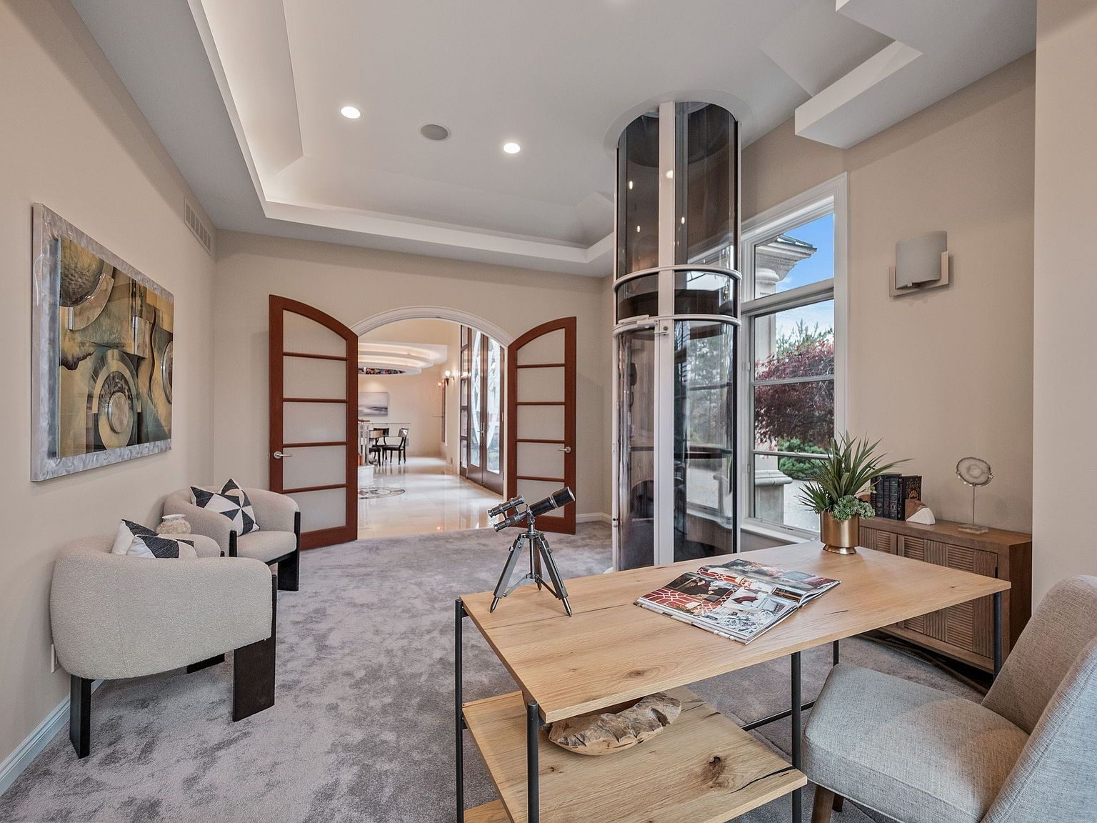 This is an interior shot of a luxurious home office. The room features a modern elevator, a wooden desk with a telescope, and comfortable seating. The color palette is neutral, creating a sophisticated and inviting atmosphere, perfect for a productive workspace.