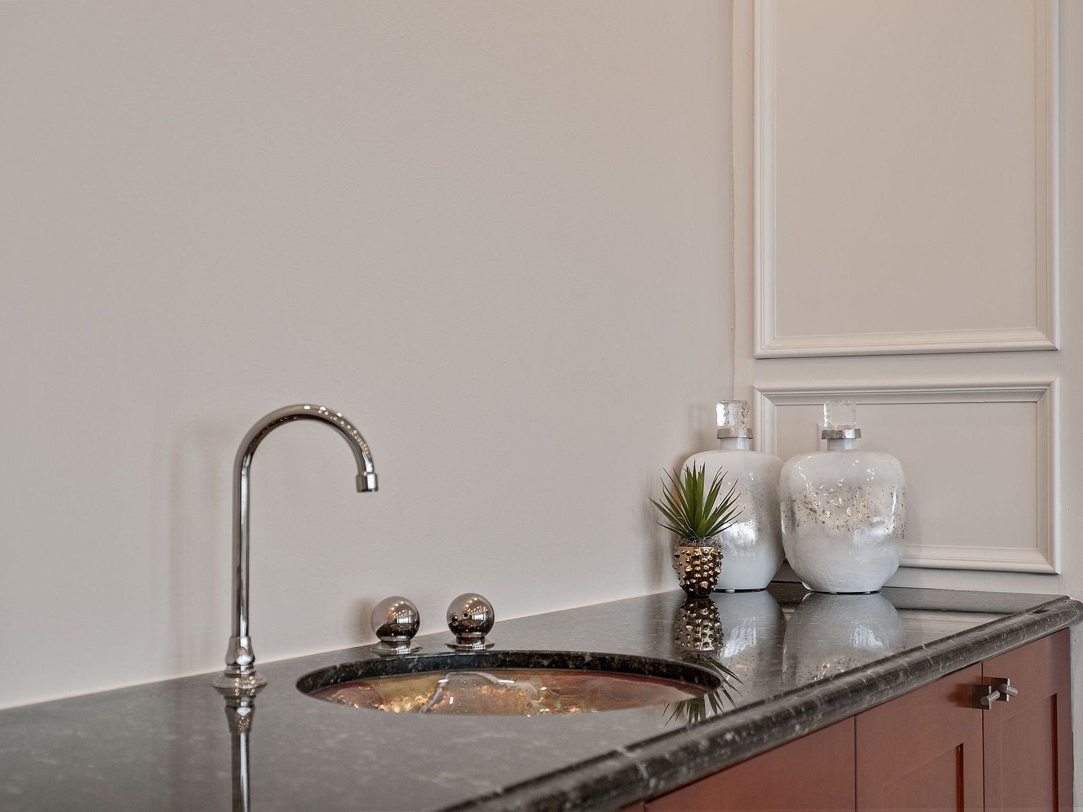 This image showcases a stylish bathroom vanity area. The dark countertop contrasts with the light walls and cabinetry, while a modern faucet and decorative bottles add a touch of elegance. The overall impression is clean, sophisticated, and well-maintained, making it an attractive feature for potential buyers.