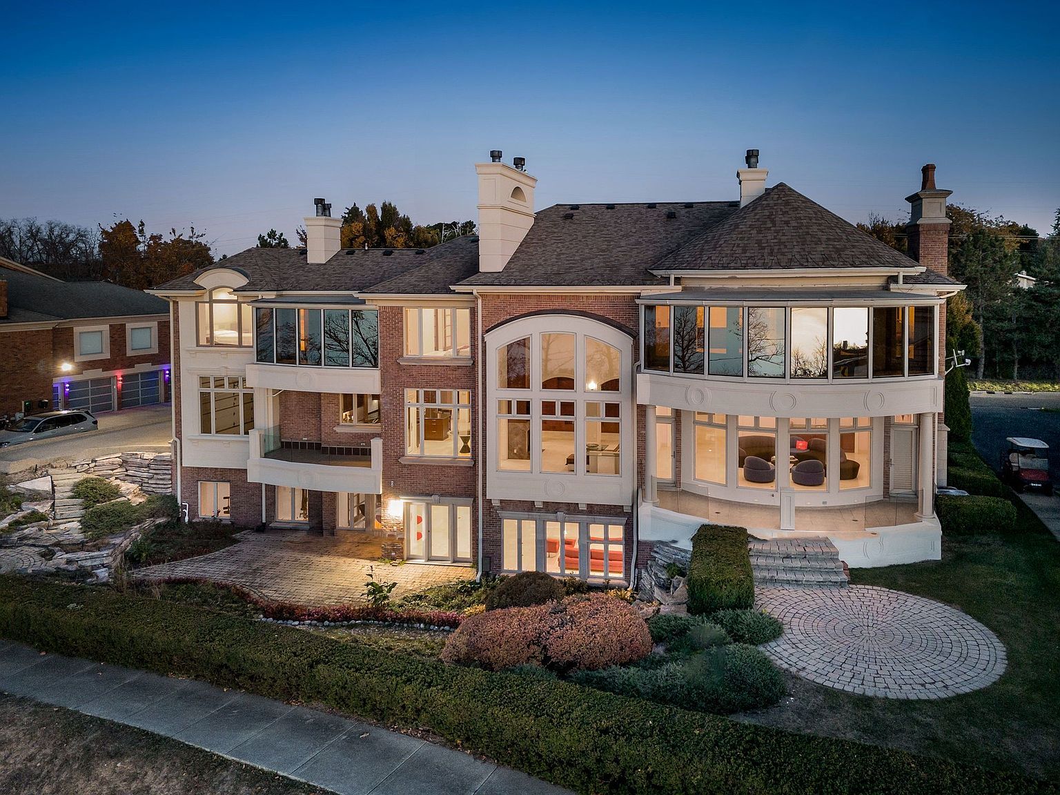This aerial view showcases a grand, multi-story brick home with a complex roofline and multiple chimneys. Large windows provide ample natural light, and a well-manicured garden and patio area enhance the property's curb appeal. The overall impression is one of luxury and sophistication.