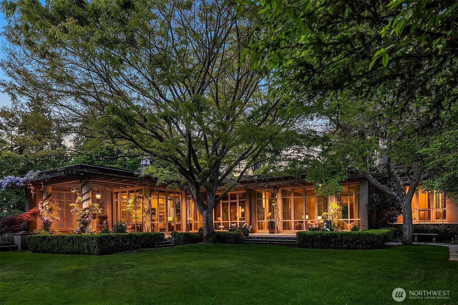 This is a rear view of a luxurious home, showcasing a seamless blend of indoor and outdoor living. The expansive glass windows and doors provide ample natural light and offer stunning views of the meticulously maintained lawn and garden. The architecture emphasizes a connection with nature, creating a serene and inviting atmosphere.