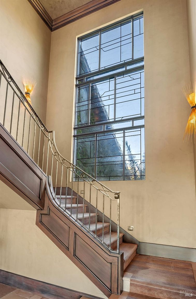 This interior shot showcases a grand staircase with a decorative metal railing and wooden accents. A large, multi-paned window provides ample natural light, complemented by sconces on the walls. The overall impression is one of elegance and architectural detail, highlighting the home's sophisticated design.