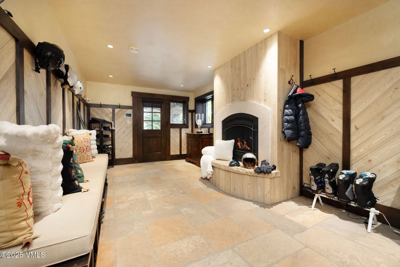 This is a cozy entryway or hallway designed for a mountain home, featuring ski equipment storage. A stone fireplace with a wooden mantel adds warmth, while wooden plank walls and a bench provide seating and storage. This space is functional and stylish, perfect for welcoming guests after a day on the slopes.