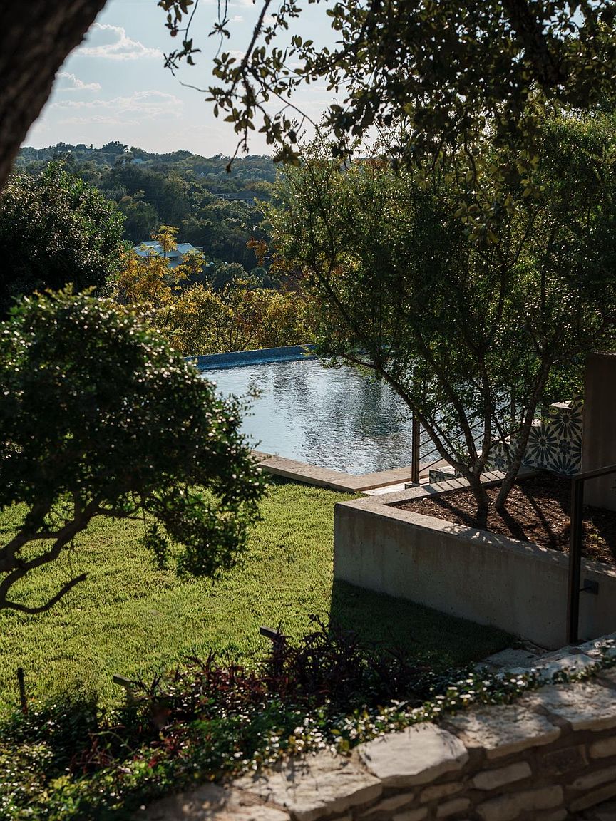 This image showcases a luxurious infinity pool overlooking a lush, green landscape. The pool's design seamlessly blends with the natural surroundings, creating a serene and private oasis. A stone retaining wall and mature trees add to the property's charm and exclusivity.