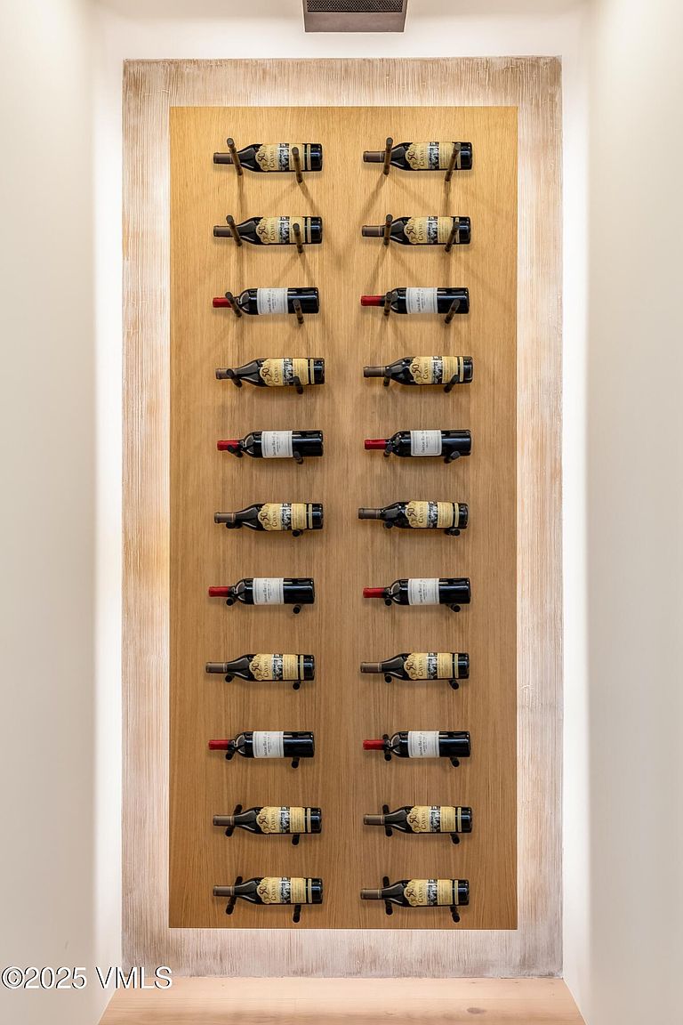 This image showcases a sophisticated, wall-mounted wine display featuring twenty bottles arranged in two vertical columns on a light wood panel. The display is framed by recessed lighting on both sides, creating a warm, glowing effect that highlights the collection. The minimalist design and symmetrical arrangement provide a clean, modern aesthetic suitable for a high-end home.