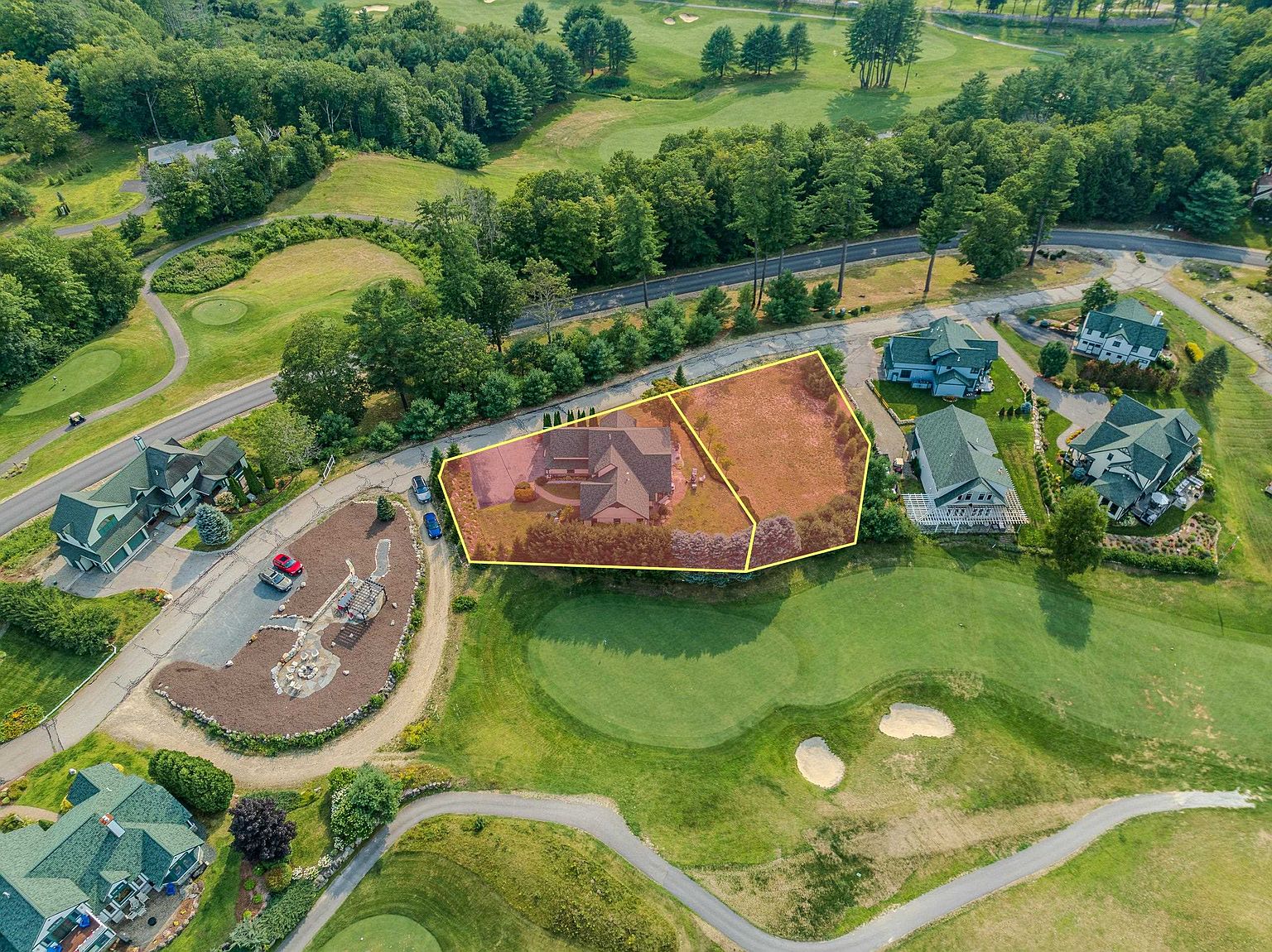This high-angle aerial view captures a residential property situated directly adjacent to a lush golf course. The highlighted lot features a single-family home with an attached garage and an adjacent undeveloped parcel, surrounded by mature trees and paved roads. The perspective emphasizes the home's prime location within a quiet, scenic neighborhood.