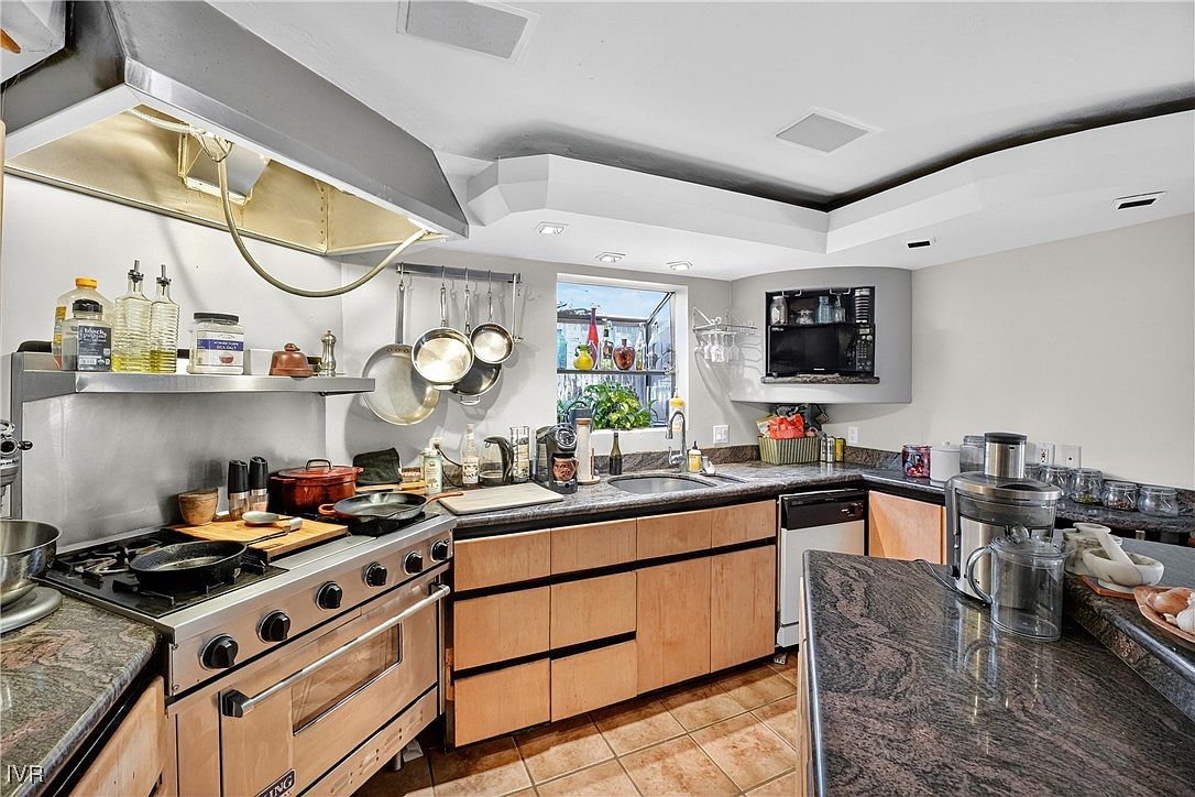 This is a well-equipped kitchen featuring stainless steel appliances, including a Viking range and a professional-grade vent hood. The countertops are granite, and the cabinets are a light wood tone. The kitchen also has a window providing natural light and a built-in television.