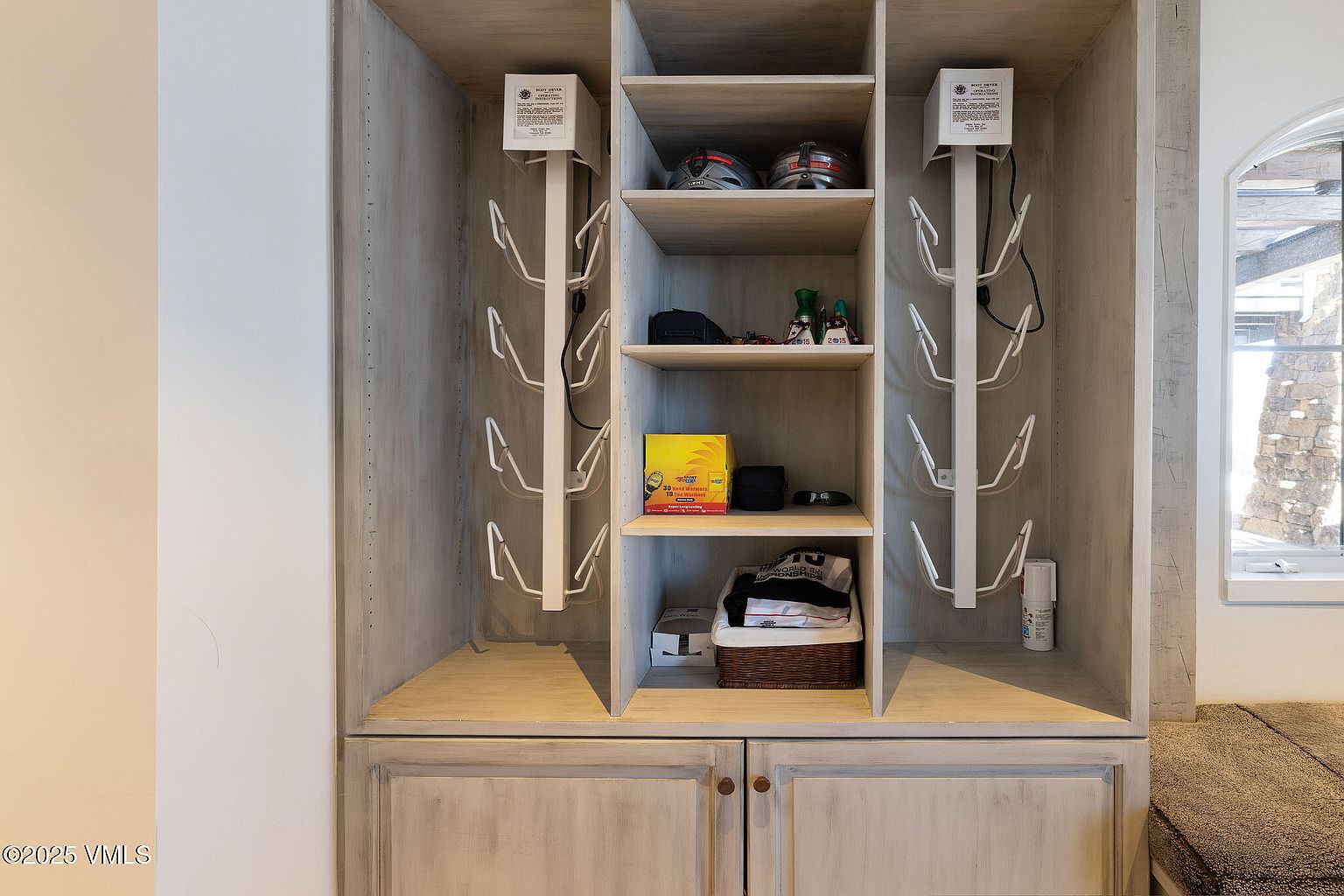 This image showcases a well-organized walk-in closet with custom shelving and storage solutions. The closet features dedicated spaces for helmets, accessories, and folded clothing, with a built-in boot dryer system on either side. The neutral color palette and efficient design create a functional and aesthetically pleasing space.