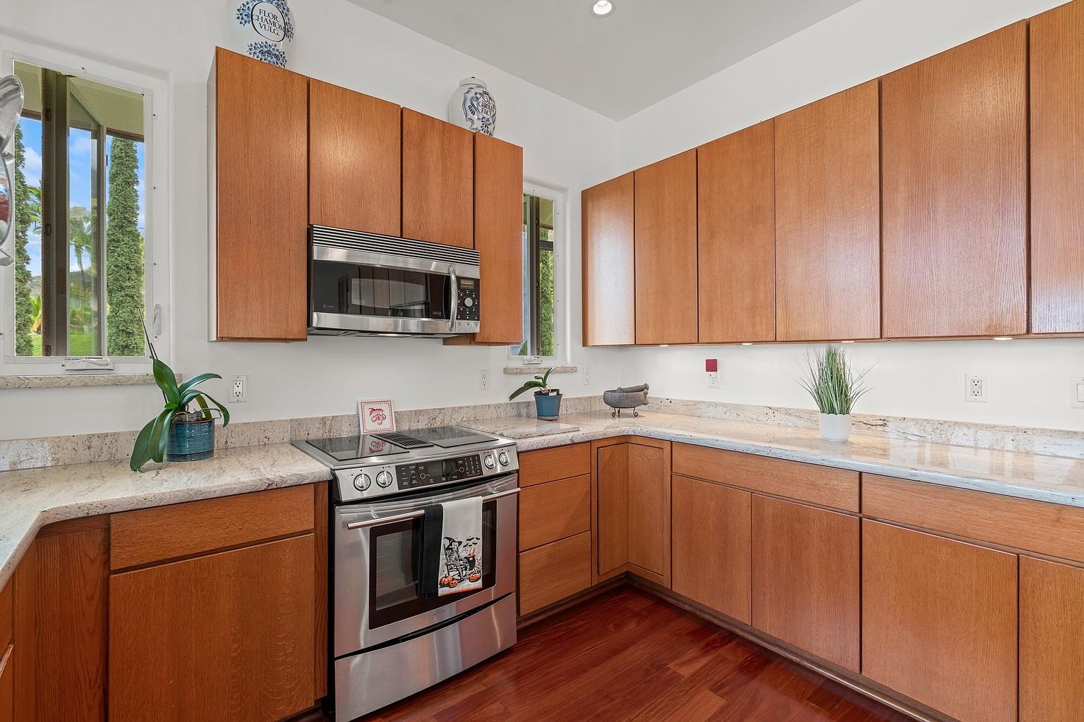 This is a well-lit kitchen featuring wooden cabinets, granite countertops, and stainless steel appliances. The kitchen has a warm and inviting feel, with natural light coming in from the windows. The hardwood floors add a touch of elegance to the space.