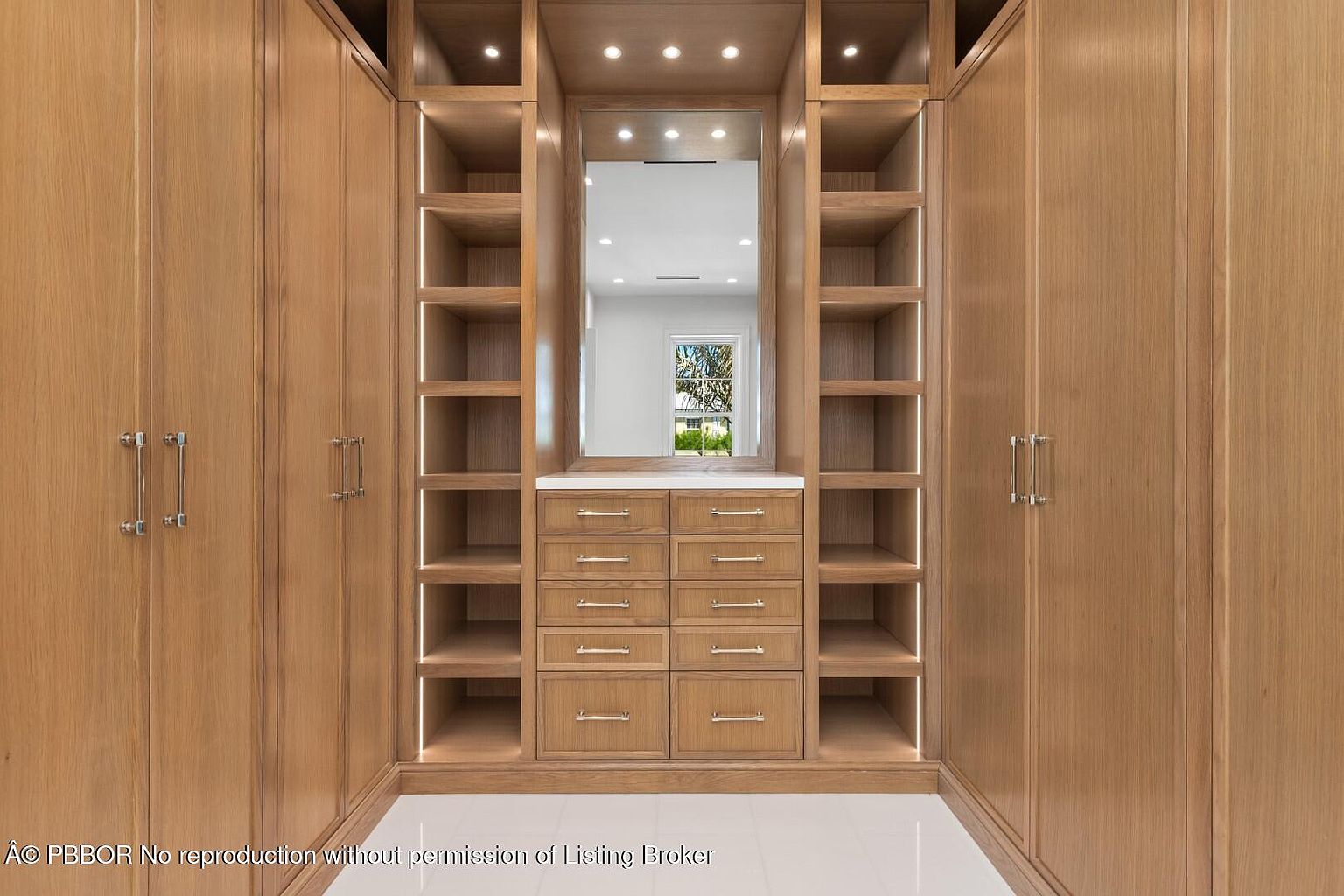 This is a well-organized walk-in closet featuring custom wood cabinetry with ample shelving, drawers, and wardrobe space. A central mirror and integrated lighting enhance the functionality and aesthetic appeal. The closet's design maximizes storage while maintaining a clean and luxurious feel.