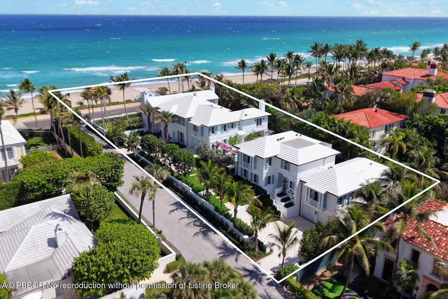 This aerial view showcases a luxurious beachfront property with multiple white buildings featuring white tile roofs, surrounded by lush tropical landscaping. The property is bordered by a pristine beach and the ocean, offering stunning views and a sense of exclusivity. The architectural style is elegant and coastal, perfect for high-end real estate.
