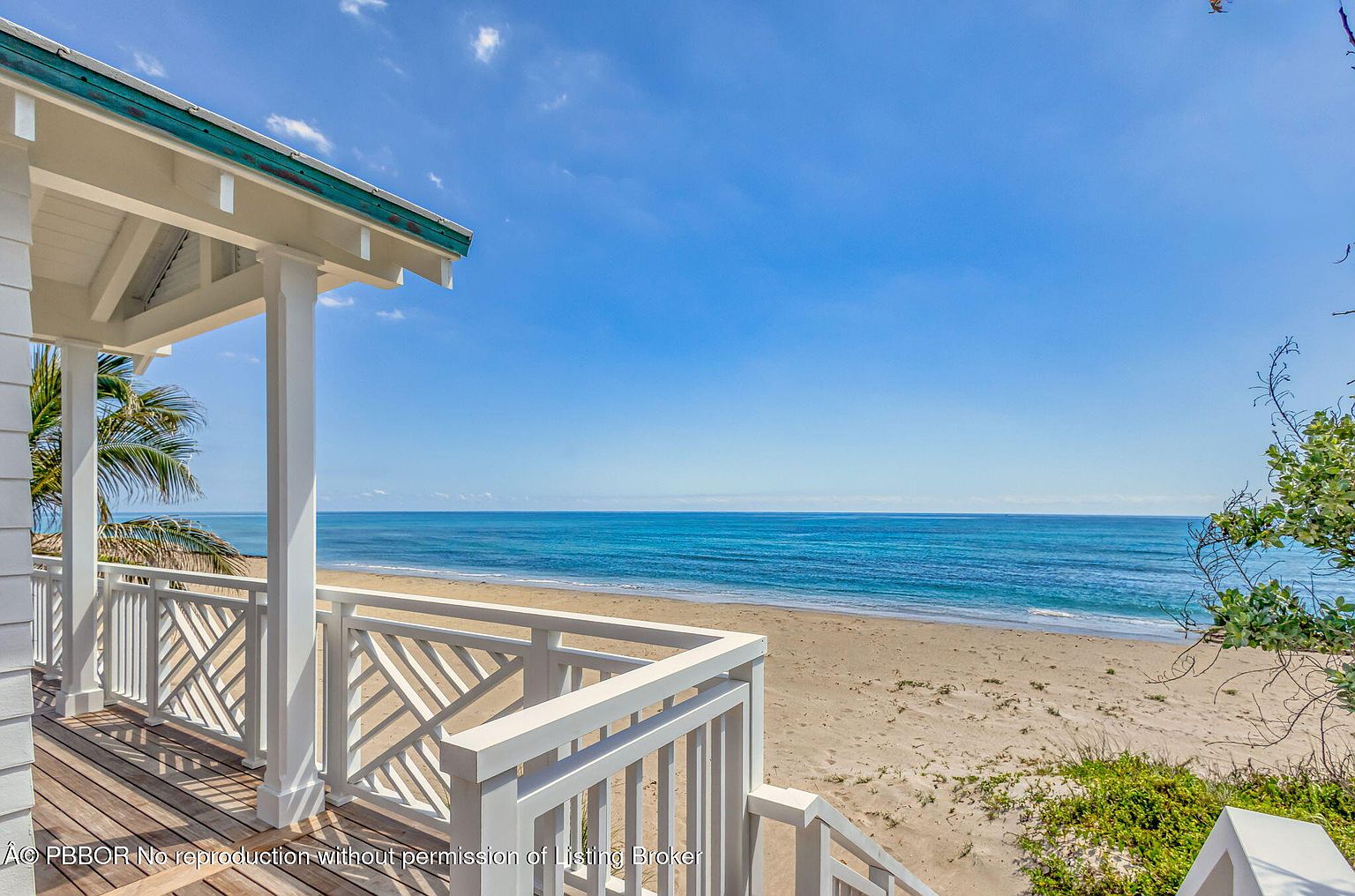 This image showcases a beautiful beachfront property from the perspective of a patio or deck. The white railing and wooden deck offer a clean, inviting space to enjoy the ocean view. The turquoise water and sandy beach create a serene and luxurious atmosphere, perfect for relaxation and outdoor living.