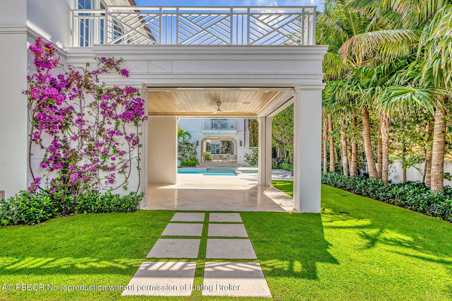 This image showcases a beautifully landscaped backyard featuring a covered patio area that leads to a swimming pool. Lush green grass and meticulously maintained hedges surround the space, while a stone pathway adds a touch of elegance. The overall impression is one of tranquility and luxury, perfect for outdoor relaxation and entertainment.