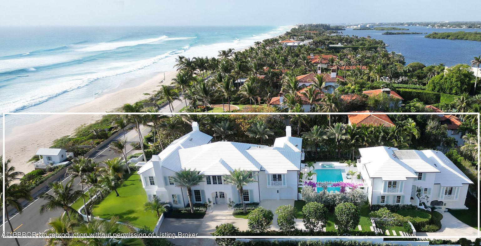 This aerial view showcases a luxurious beachfront property with a pristine white exterior, complemented by lush green lawns and mature palm trees. A sparkling blue pool adds to the resort-like ambiance, while the ocean and waterway provide stunning backdrops. The overall impression is one of opulence and coastal elegance.
