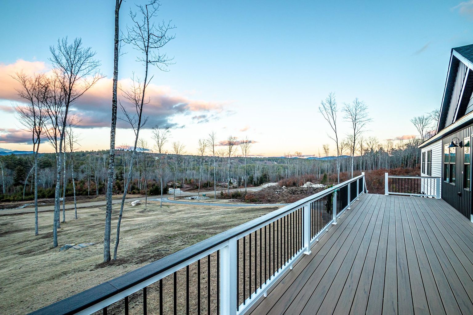This image showcases a spacious, modern deck with composite wood-look decking and a sleek white railing with black balusters. The perspective looks out over a vast, open landscape of rolling hills and sparse trees under a soft, twilight sky. The clean lines and expansive view create an inviting atmosphere perfect for outdoor relaxation and entertaining.