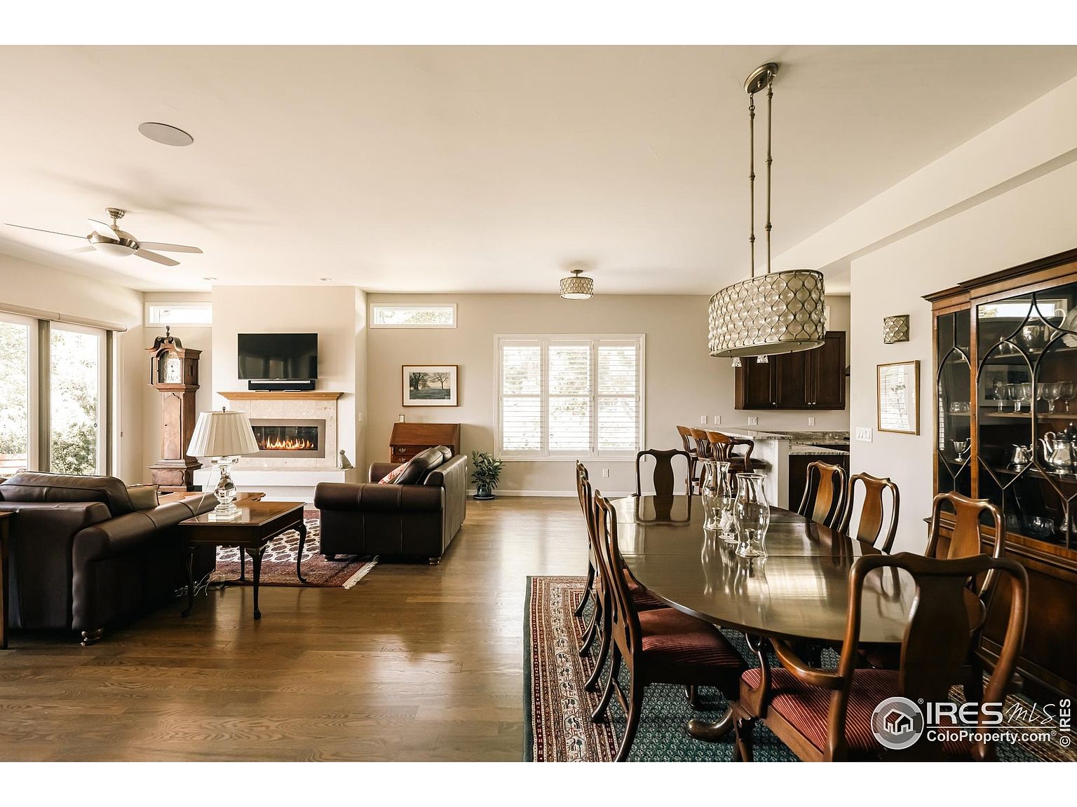 This interior shot showcases a spacious dining room adjacent to a living area. The dining room features a large oval table with seating for eight, illuminated by a decorative chandelier. A dark wood china cabinet adds a touch of traditional elegance, while the hardwood floors and neutral wall colors create a warm and inviting atmosphere.