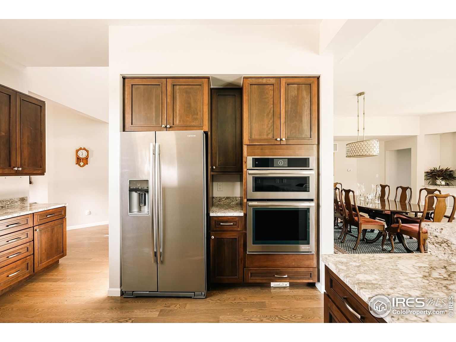 This interior shot showcases a well-appointed kitchen with rich wood cabinetry and stainless steel appliances, including a large refrigerator and built-in oven/microwave combo. The granite countertops complement the warm tones of the wood, while the hardwood flooring adds to the overall elegance. The kitchen seamlessly transitions into a dining area, creating an open and inviting space.
