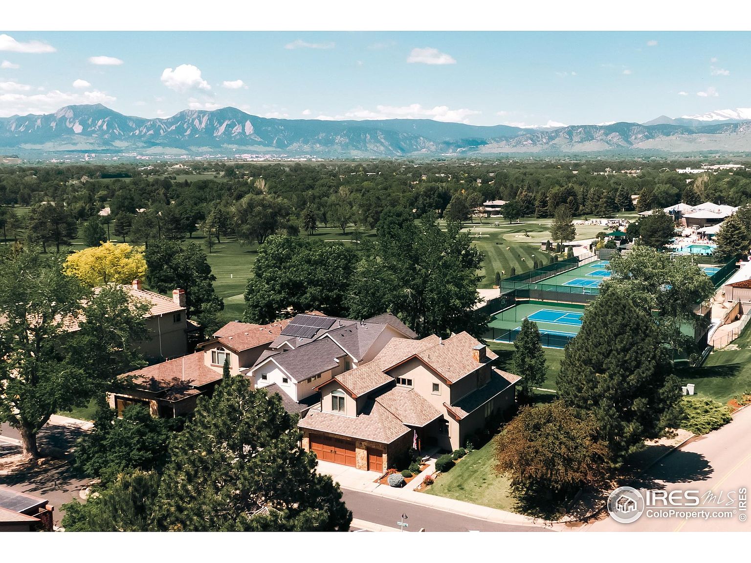 This aerial view showcases a residential neighborhood nestled near a golf course and tennis courts, with a stunning mountain range in the background. The homes feature varied architectural styles and well-maintained landscaping, creating an appealing and upscale community. The image highlights the desirable location and recreational amenities available to residents.
