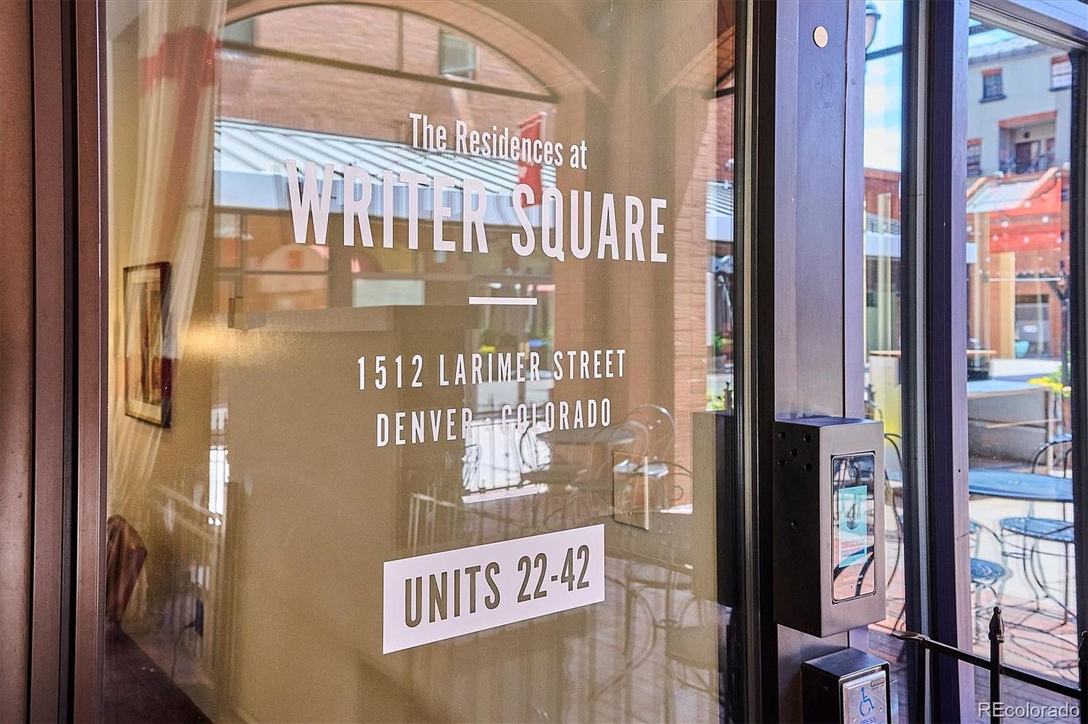 The image captures the entryway of "The Residences at Writer Square," located at 1512 Larimer Street, Denver, Colorado. The glass door displays the building's name and address, along with the unit range of 22-42. An intercom system is visible on the right side of the door, suggesting a secure entry point.