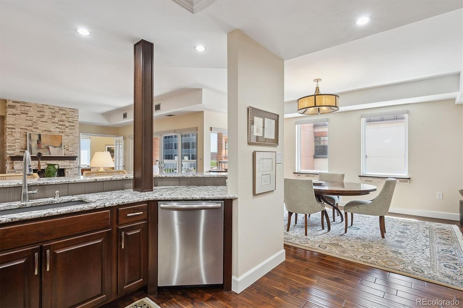 This interior shot showcases a well-appointed kitchen and dining area. The kitchen features dark wood cabinetry, granite countertops, and stainless steel appliances, while the adjacent dining area includes a round table with upholstered chairs, illuminated by a modern chandelier. The hardwood flooring and neutral wall colors create a warm and inviting atmosphere.
