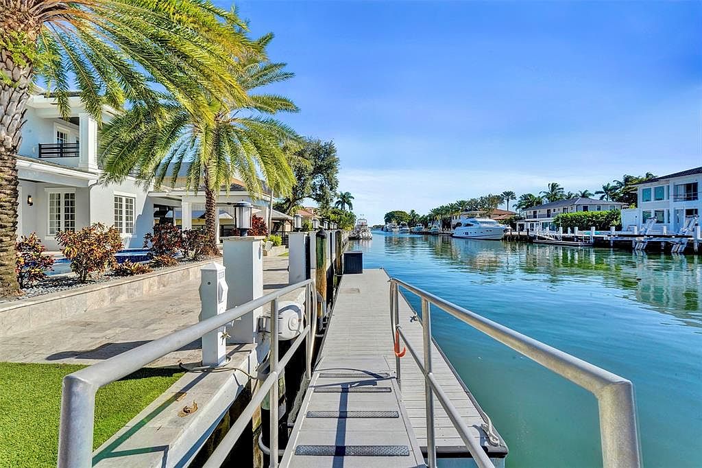 This image showcases a waterfront property with a private dock extending into a canal. The dock features railings and a walkway, offering direct access to the water. Luxurious homes line the canal, complemented by lush palm trees and clear blue skies, creating an inviting and upscale atmosphere.