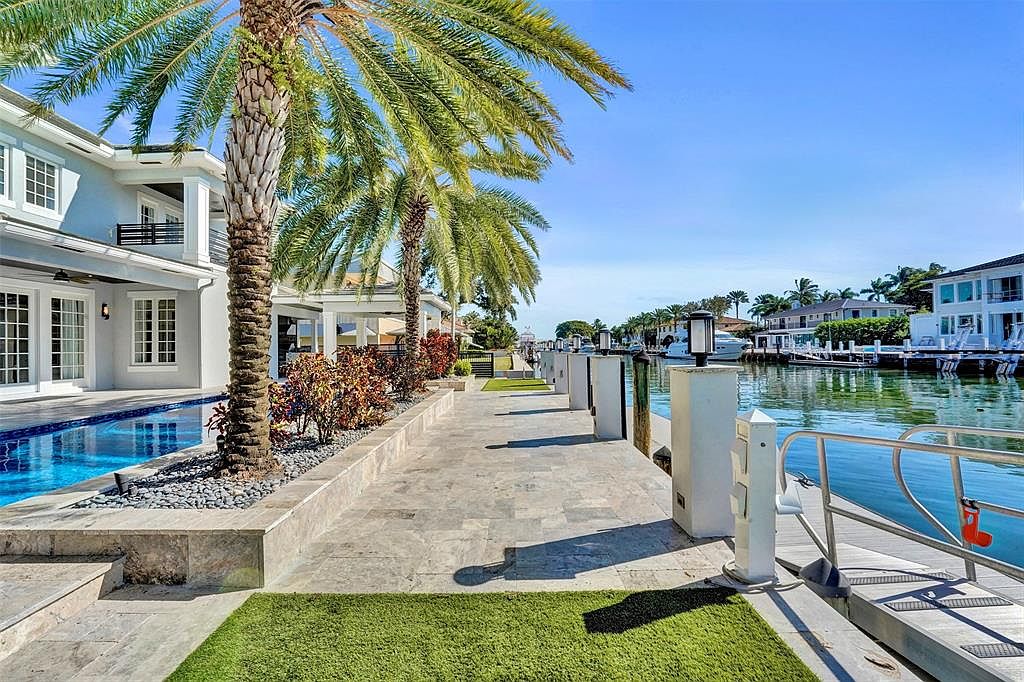 This image showcases a luxurious waterfront property featuring a stunning pool and dock area. The pool is adjacent to the house, while the dock extends into the canal, lined with palm trees and manicured landscaping. The scene exudes a sense of upscale coastal living, perfect for relaxation and entertaining.
