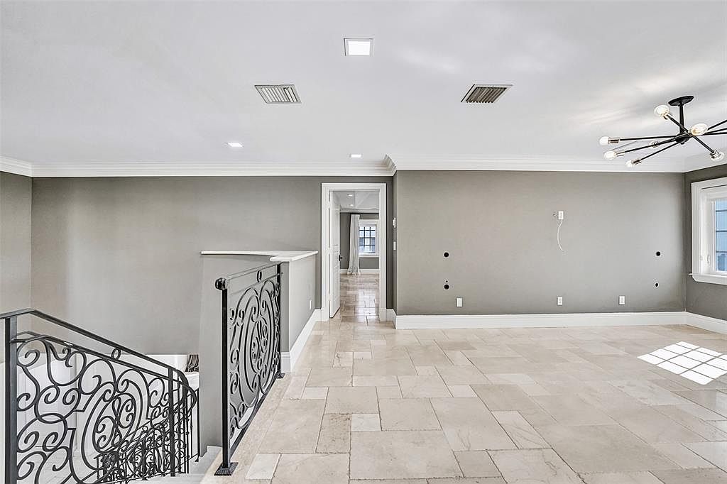 This interior shot showcases a hallway and staircase area with a neutral color palette. The walls are painted a soft gray, complemented by white trim and a light-colored tile floor. A decorative wrought iron railing adds an elegant touch to the staircase, while a doorway leads to another room, creating a sense of depth and flow.