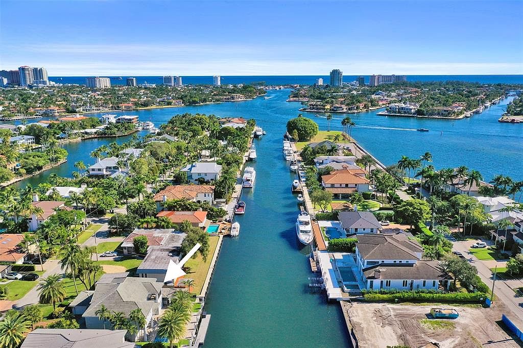 This aerial shot showcases a luxurious waterfront property nestled along a canal. The house features a well-manicured lawn, mature palm trees, and a private dock, offering direct access to the waterway. The surrounding neighborhood is characterized by similar high-end homes and lush landscaping, creating an exclusive and desirable residential area.