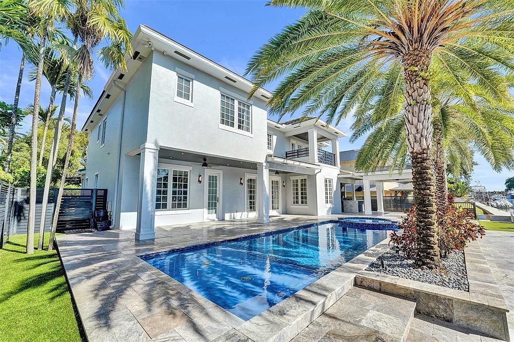 This image showcases the rear exterior of a luxurious two-story home, highlighting a stunning rectangular pool with a spa. The pool is surrounded by a stone patio and lush landscaping, including mature palm trees. The architecture features clean lines, large windows, and a covered patio area, creating an inviting outdoor living space.